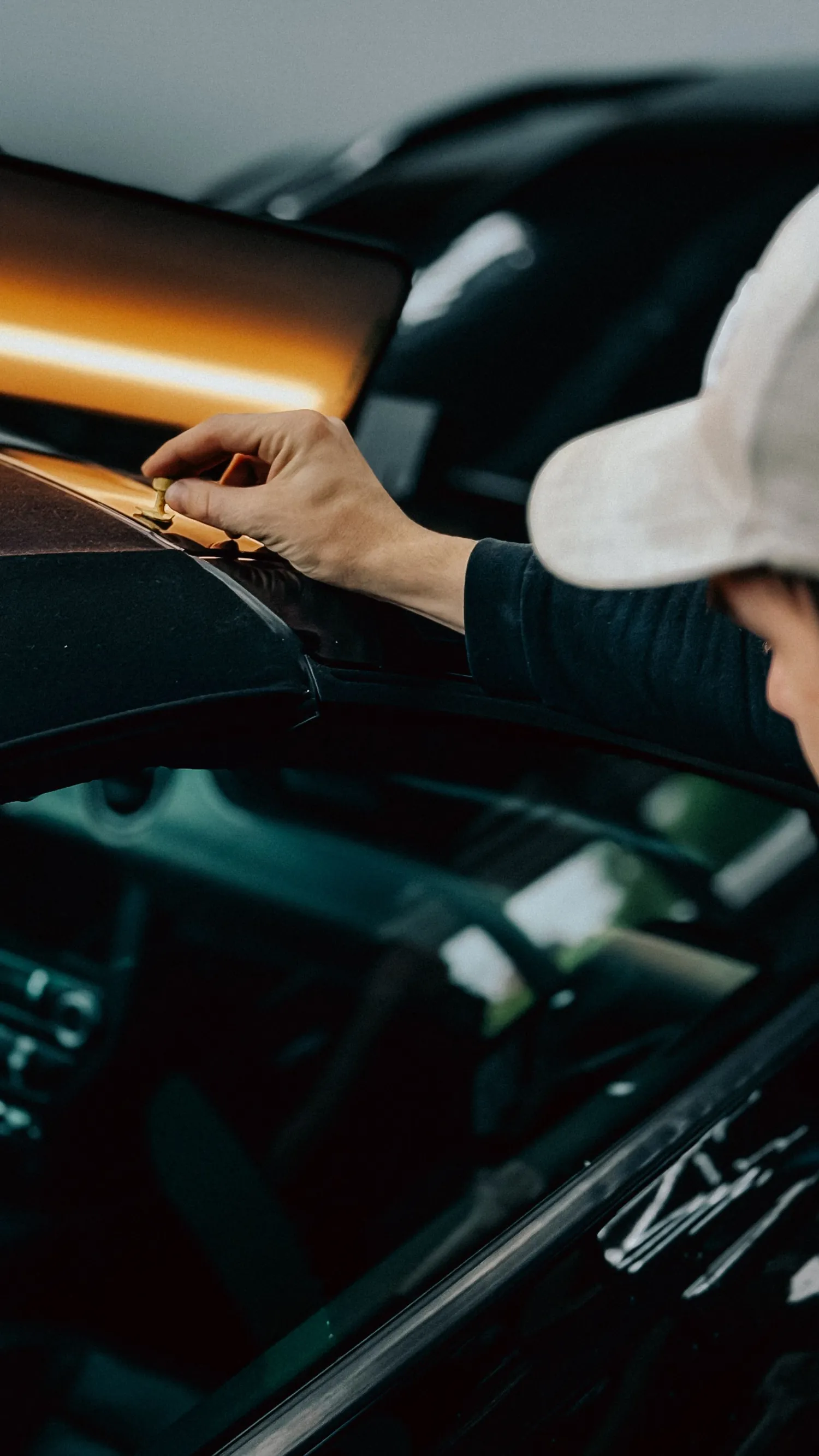 Mão de instalador ajustando a película sobre a pintura de um carro escuro, com luz quente de aquecimento